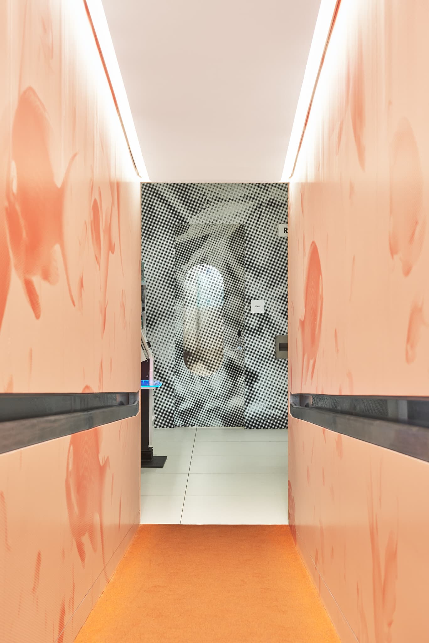 Orange halftone fish mural in the tunnel ramp leading from the kids area to the lobby area, with the grayscale halftone info desk flower mural visible at the end