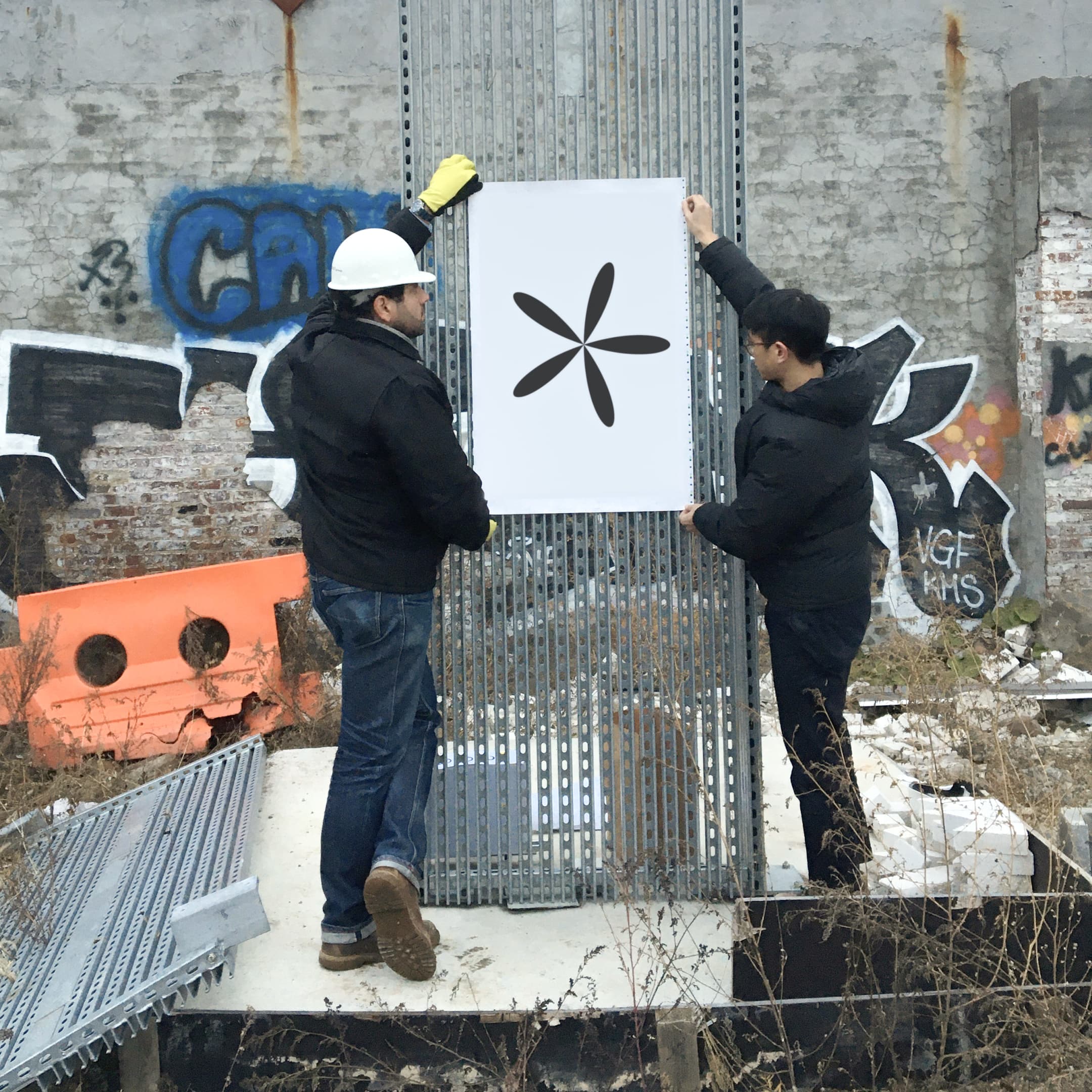 Two people stand holding a poster with the fleuron up to the fence.