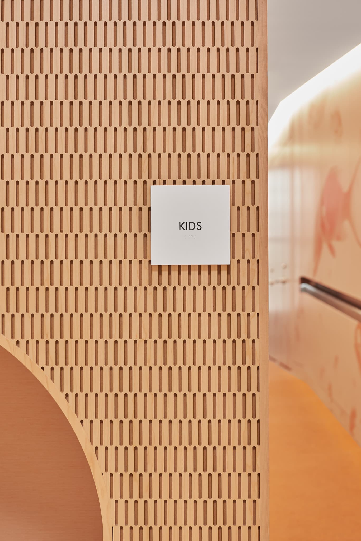 Closeup of the "Kids" sign next to the access tunnel to the kids area, with braille